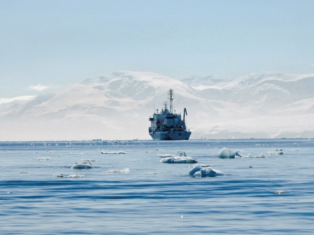 Ein Schiff fährt zwischen kleinen Eistrümmern auf die antarktische Küste zu.
